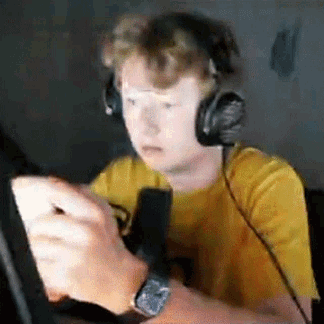 a young man wearing headphones and a watch is playing a video game on his phone .