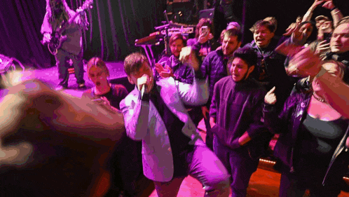 a man singing into a microphone with a crowd behind him