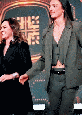 a woman in a suit stands next to another woman in a black suit