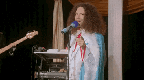 a man with curly hair is singing into a microphone while playing a keyboard .