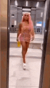 a woman in a pink dress is standing in an elevator looking at herself in the mirror .
