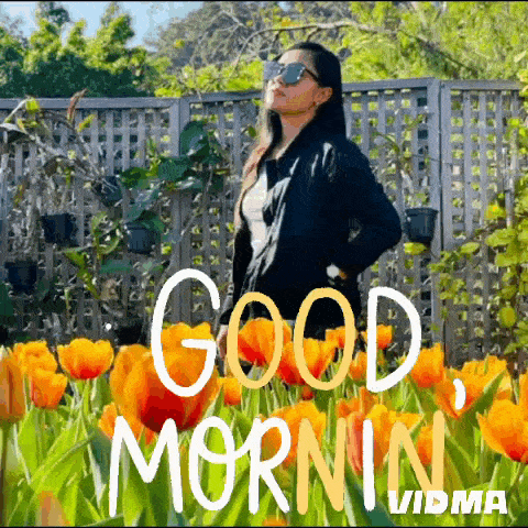 a woman wearing sunglasses is standing in a field of orange flowers .