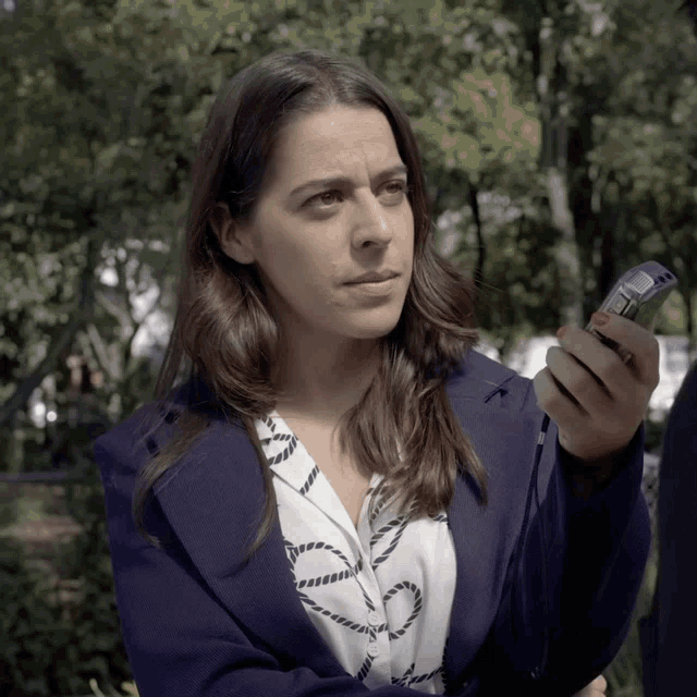 a woman in a blue jacket is holding a cell phone in her hand