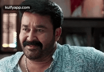 a man with a beard and mustache is smiling while wearing a blue shirt .