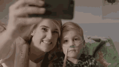 a woman is taking a selfie with a young boy with an oxygen mask on his nose .