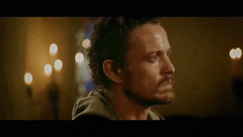 a man with a beard is standing in a dark room with candles .