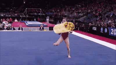 a female gymnast is holding a pizza in her hand while doing a trick on the floor
