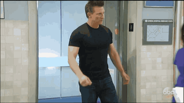a man in a black shirt stands in front of an elevator with a sign that says general hospital emergency exits