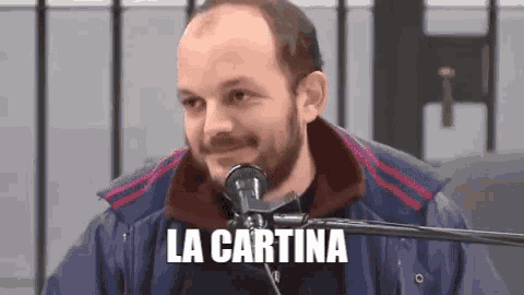 a man with a beard is sitting in front of a microphone with the words la cartina written on it .