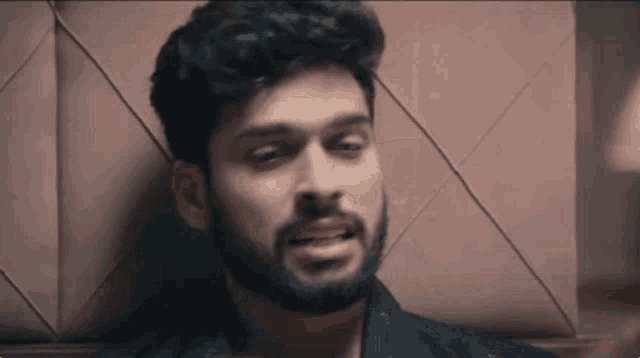 a man with a beard is leaning against a wall and making a face .