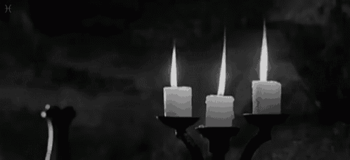 a black and white photo of three candles burning in a candelabra .