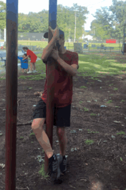 a man in a red shirt is leaning on a pole
