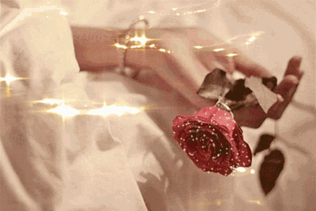 a woman 's hand is holding a red rose with glitter on it