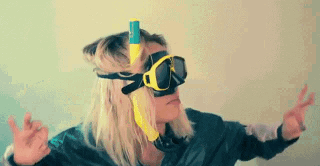 a woman wearing a diving mask and goggles is making a peace sign with her hands .