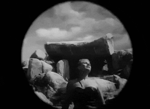 a woman is standing in front of a large rock .