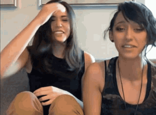 two women are sitting next to each other on a couch and one of them is scratching her head .