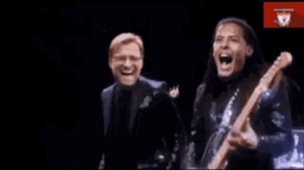 a man is holding a guitar and another man is laughing .