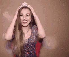a woman wearing a tiara is smiling and holding her hair .