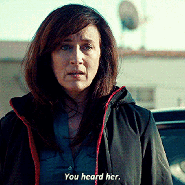 a woman in a black jacket says " you heard her " in front of a car