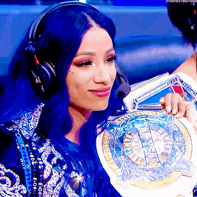 a woman with blue hair is wearing headphones and holding a wrestling championship belt