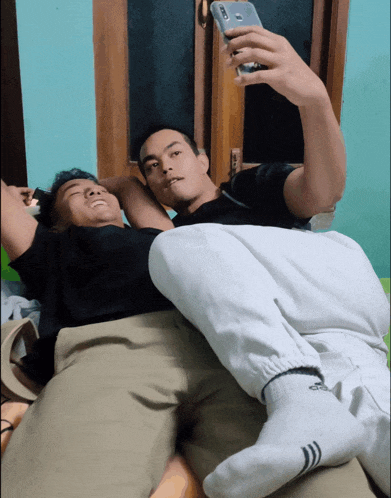 a man laying on another man 's lap taking a selfie with his phone