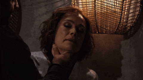 a man holds a woman 's neck in a dark room with a lamp in the background