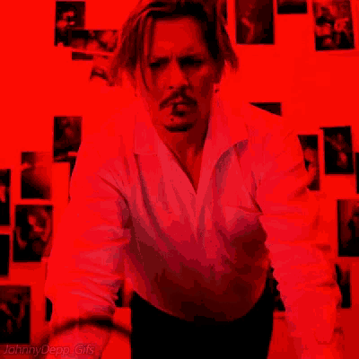 a man in a white shirt is smoking a cigarette in front of a red wall .