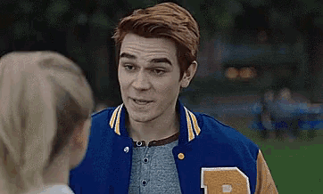 a man in a blue and brown varsity jacket is talking to a girl .