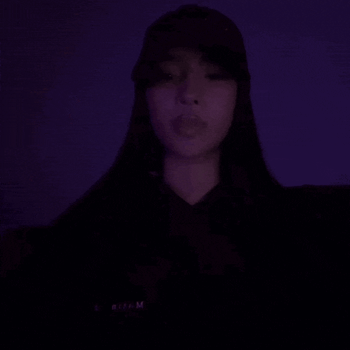 a woman in a black hat is making a heart shape with her hands in the dark .