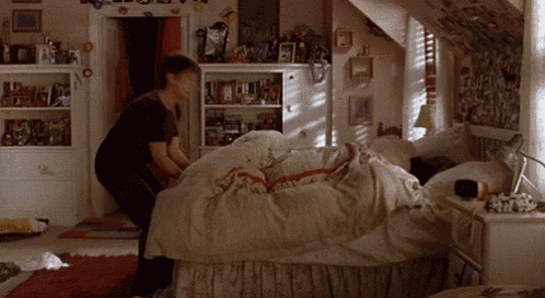 a person is making a bed in a bedroom with a lot of pictures on the walls