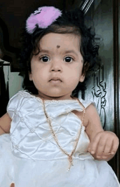 a baby girl is wearing a white dress and a pink hair clip .