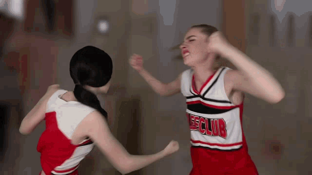 two cheerleaders are fighting with one wearing a jersey that says eeclub