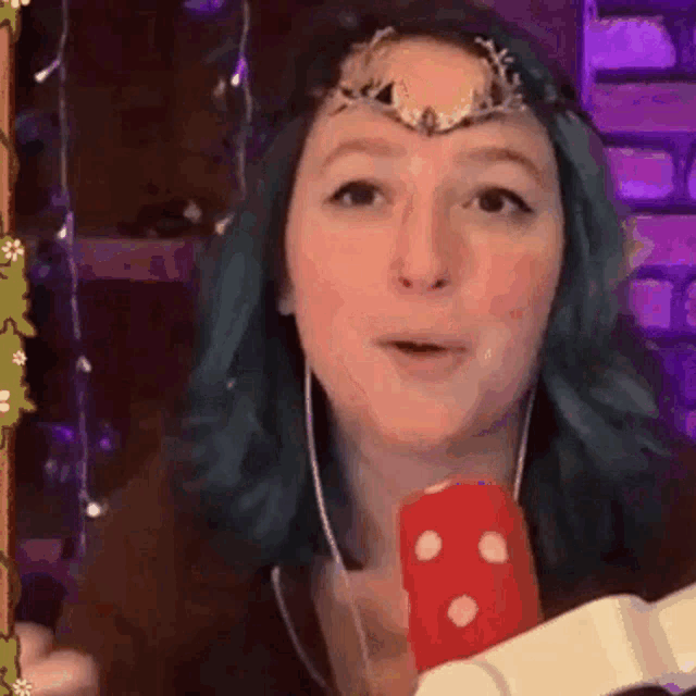 a woman with blue hair and a crown on her head is holding a microphone and a dice .