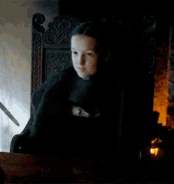 a young girl is sitting in a chair in a dark room with a candle .