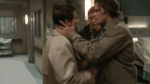 a group of men are standing in a hallway and one of them is holding another man 's face