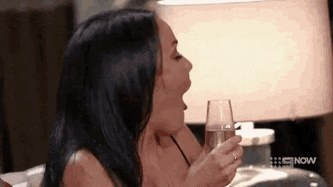 a woman is holding a glass of champagne with the word now on the bottom