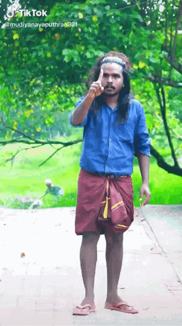 a man in a blue shirt and red skirt is standing on a sidewalk with his finger pointing up