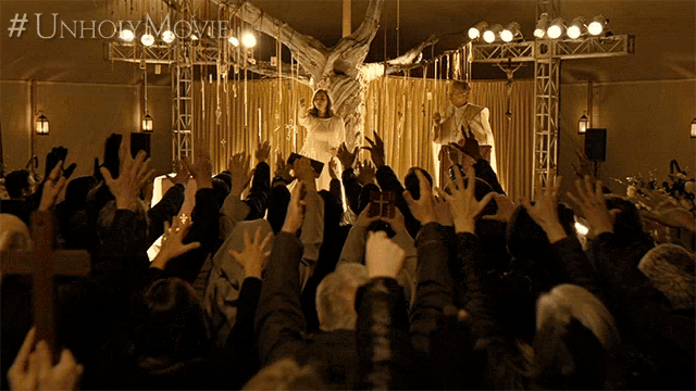 a crowd of people raising their hands in front of a statue of jesus on a cross