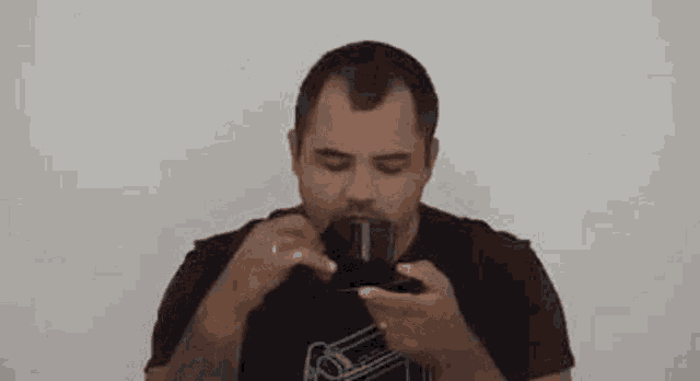a man is drinking from a cup with his eyes closed and a tattoo on his arm .