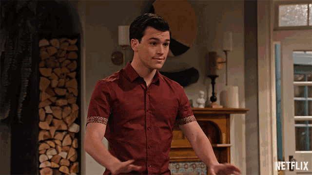 a man in a red shirt is standing in front of a fireplace with a netflix logo on the bottom right