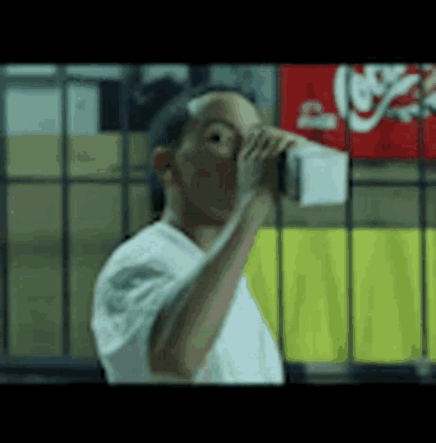 a man in a white shirt is drinking from a bottle while standing in front of a coca cola sign .