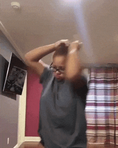 a woman wearing glasses is dancing in a room with a tv on the wall