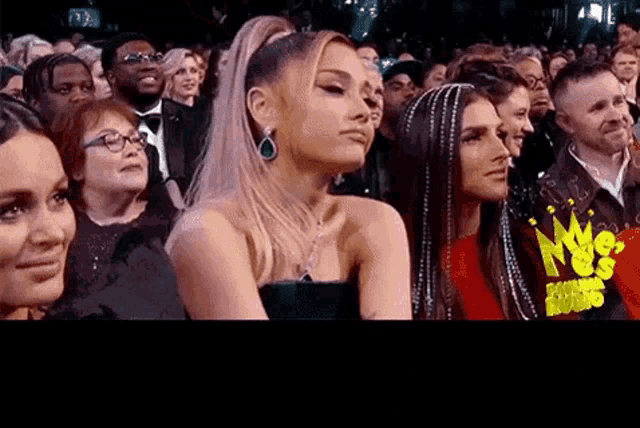 ariana grande is sitting in a crowd of people watching a concert .