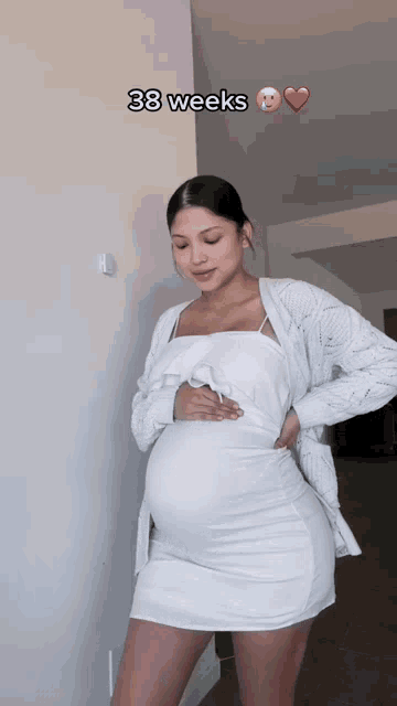a pregnant woman is wearing a white dress and a white cardigan and is 38 weeks pregnant