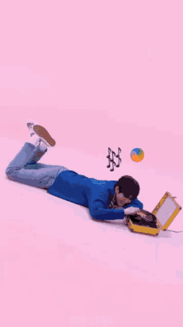 a man is laying on his stomach playing a record player on a pink background