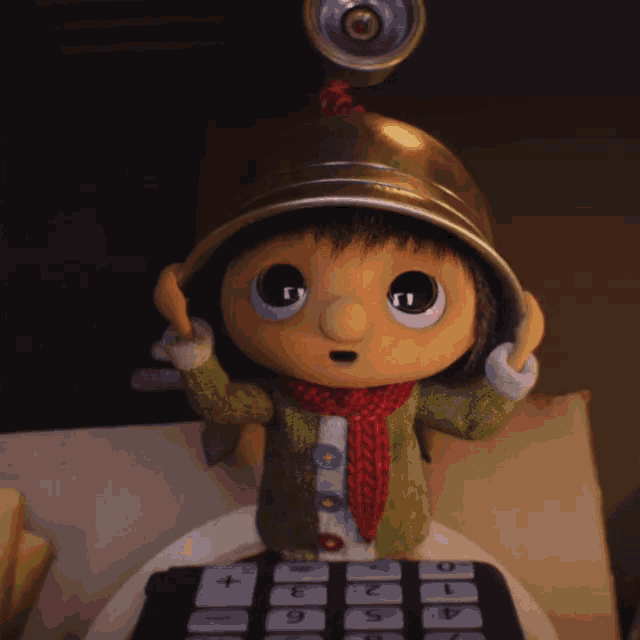 a stuffed toy wearing a helmet and a scarf sits on a calculator