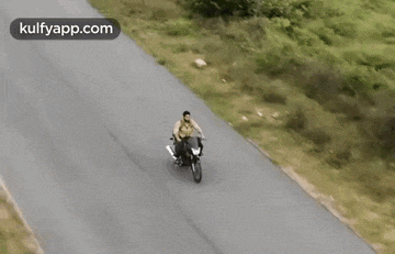 a man is riding a motorcycle down a road with the website kulfyapp.com in the corner .