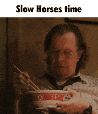 a man is eating a bowl of noodles with chopsticks and the words slow horses time above him