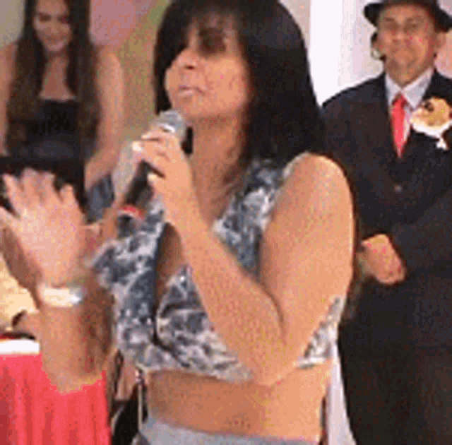 a woman in a crop top is holding a microphone in front of a group of people .