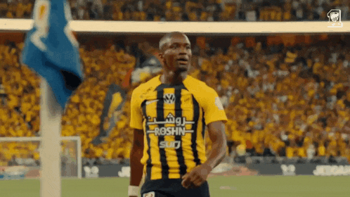 a soccer player wearing a yellow and black jersey that says roshn